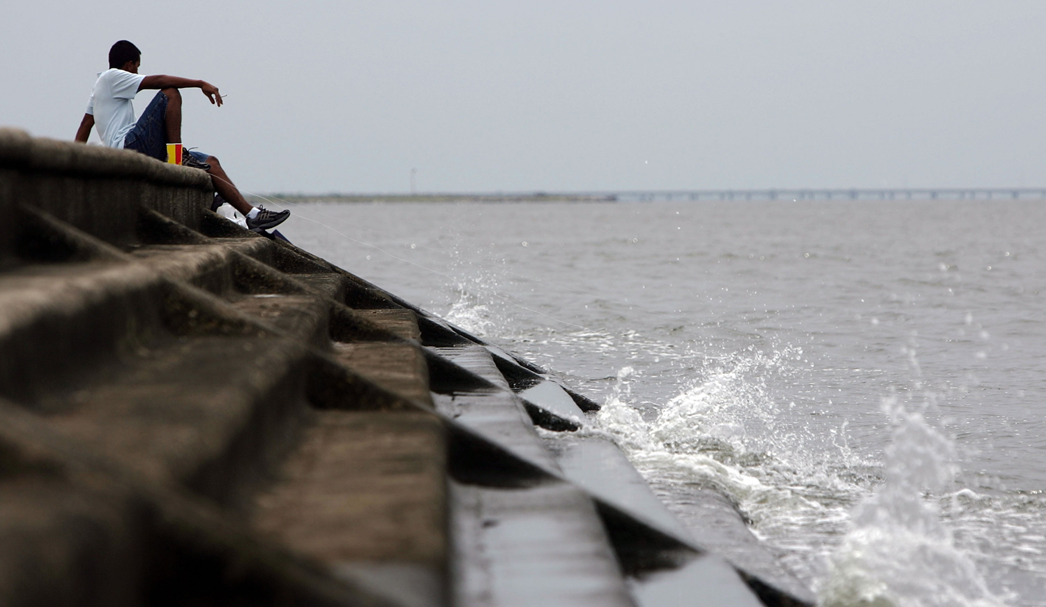 A man sits beside a levee on Lake Pontchartrain, New Orleans, La. (Credit: James Joel/ Flickr)