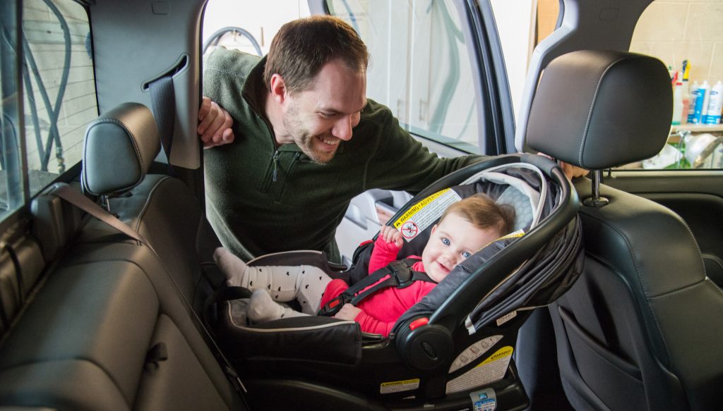 A father safely buckles his daughter into her rear facing car seat. (Credit: North Dakota DOT)